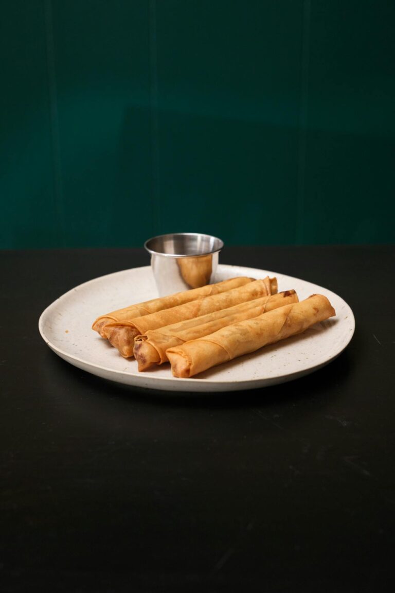A plate of golden Filipino lumpia served with dipping sauce, showcasing traditional flavors.