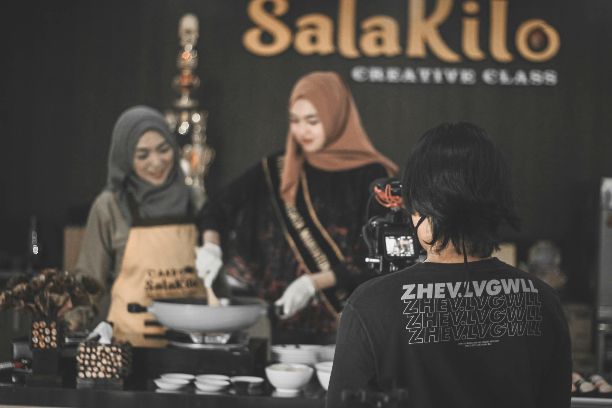 Back view of unrecognizable photographer shooting food vlog with ethnic women in hijabs cooking in modern kitchen