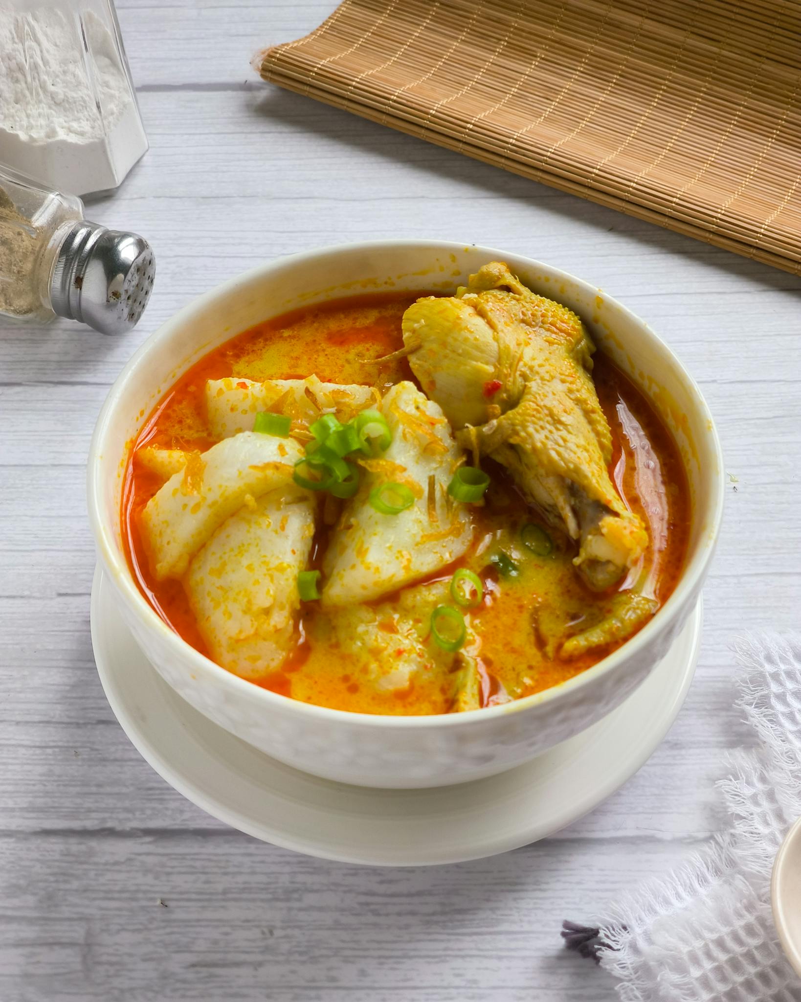 Delicious bowl of spicy chicken curry with rice cake topped with green onions.