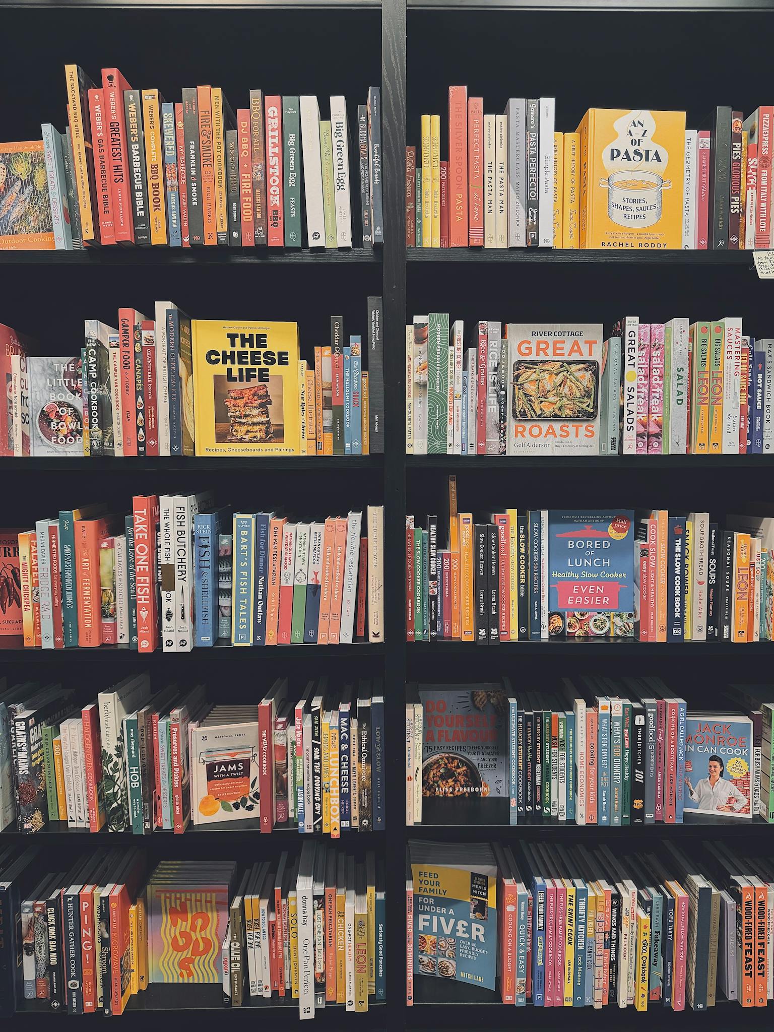 Vibrant array of cookbooks displayed on black shelves, showcasing culinary diversity.